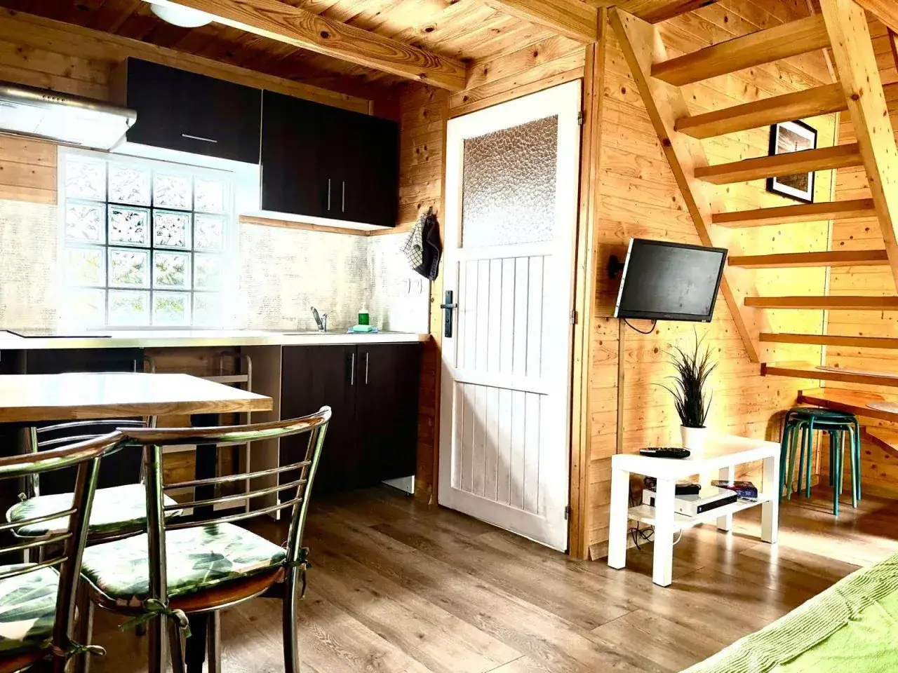 Przytulne wnętrze jednego z kolorowych domków w Jastrzębiej Górze. Drewniane ściany, kuchnia, schody na piętro i telewizor.