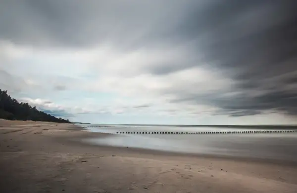 Spokojna plaża i morze, idealne na wypoczynek w ośrodku wczasowym Zacisze. Długie fale i las sosnowy tworzą malowniczy krajobraz.