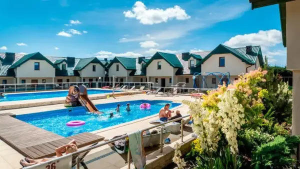 Rodzinny wypoczynek w domkach apartamentowych Fulay Premium. Dzieci bawią się w basenie ze zjeżdżalnią, dorośli relaksują się na leżakach.