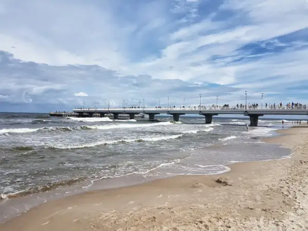 Kołobrzeg wczasy z wyżywieniem: spacer po molo, fale na plaży i tłumy turystów. Idealne miejsce na relaks nad Bałtykiem.