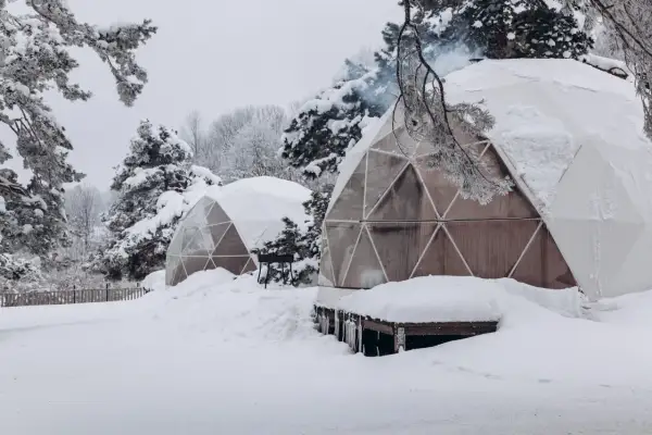 Śnieżne krajobrazy i przytulne domki do wynajęcia na weekend. Dym unosi się z komina jednego z igloo, zapraszając do środka.
