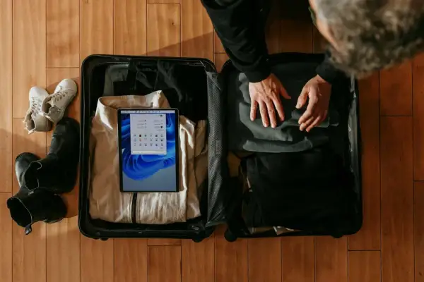 Osoba pakuje walizkę podręczną, w której widać ubrania, buty i tablet.