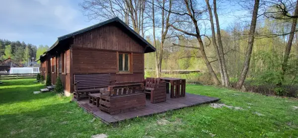 Drewniana chata z meblami na tarasie, otoczona zielenią i lasem. Idealne miejsce na agroturystykę w pobliżu.