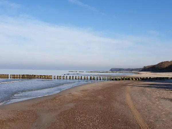 Spokojne morze i pusta plaża w Rusinowie nad morzem. Drewniane falochrony wcinają się w wodę, tworząc malowniczy krajobraz.