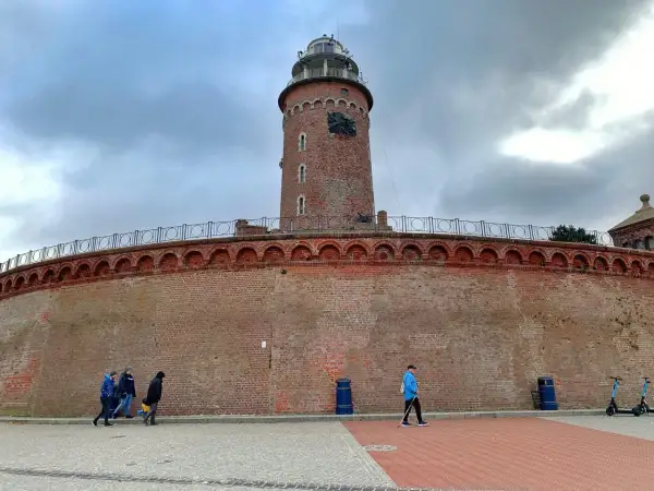 Latarnia morska w Kołobrzegu, jeden z punktów, które warto zobaczyć. Potężny ceglany fort i wieża górują nad spacerującymi.