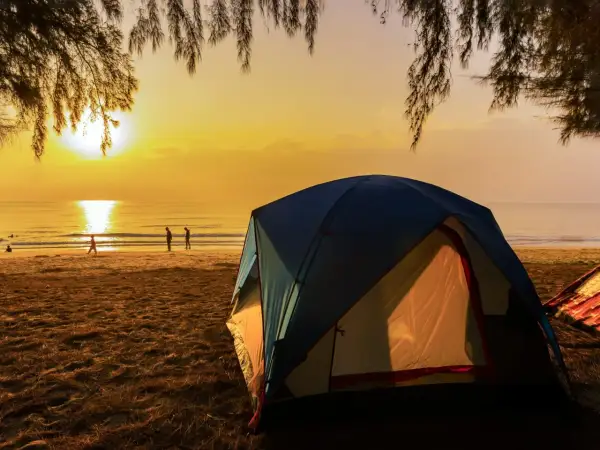 Namiot na polu namiotowym nad morzem przy plaży, gdzie słońce zachodzi, malując niebo na złoto.