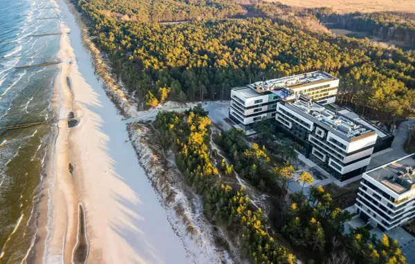 Nowoczesne budynki hotelowe w Rogowie nad morzem, otoczone sosnowym lasem, z widokiem na piaszczystą plażę i fale Bałtyku.