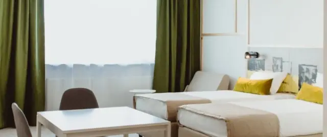 Pokój hotelowy z dwoma łóżkami, stolikiem i krzesłami. Zastanawiasz się, ile kosztuje nocleg w Warszawie?